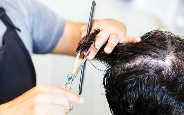 Schere und Kamm beim präzisen Schneiden dunkler Haare