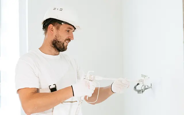 Ein Mann mit Schutzhelm arbeitet an Leitungen in einem Neubau