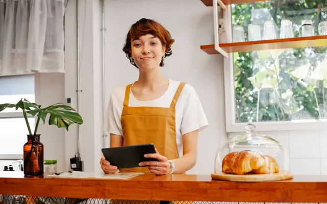 Eine lächelnde Frau mit Schürze an einer Cafétheke mit Gebäck