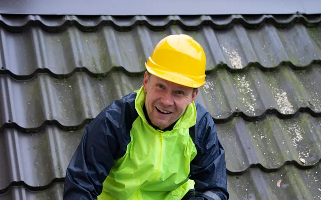Ein lächelnder Mann mit Schutzkleidung bearbeitet Dachmaterial