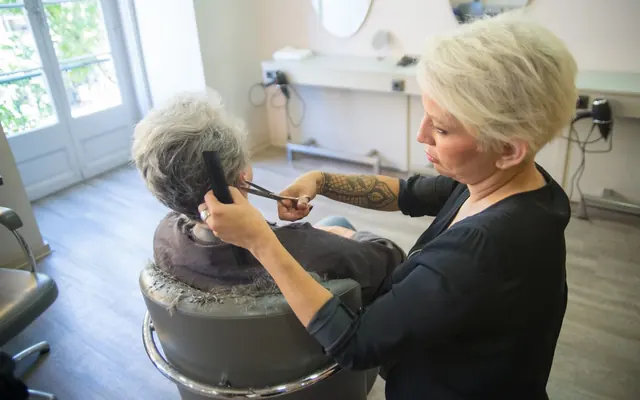 Eine Frau schneidet mit Schere und Kamm Haare in einem hellen Salon